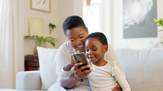 A mum and son sat on the sofa smiling together looking at and engaging with something, maybe an educational app, on a mobile phone.