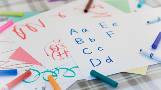 A table with felt tip pens and lots of children's drawings underneath hand written letters A-F.