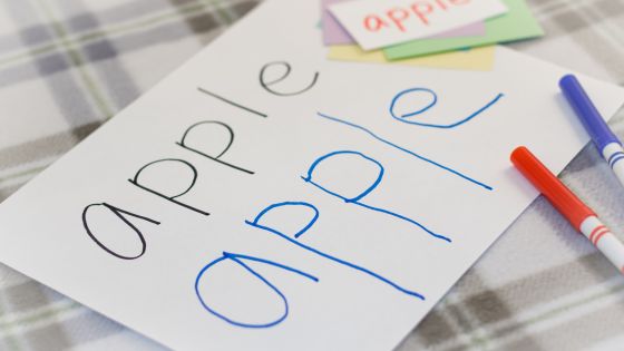A piece of paper on the table with the word apple twice where children have copied the english vocabulary word.