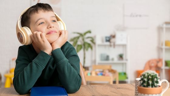 A boy sat at a desk smiling as he listens to something via his wireless headset.