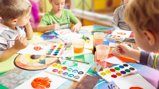 A picture of children sat around a circular table painting apples with watercolours.