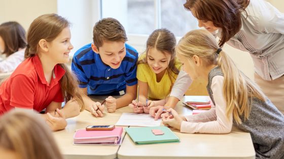four children sat a table together with a teacher looking at a workbook.