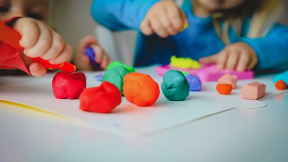 Two children playing with different coloured balls of playdough at a table.