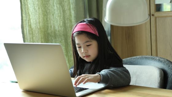 A girl sat at a desk using a laptop.