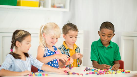 Four children are around a table making jewellery with a range of colourful beads.