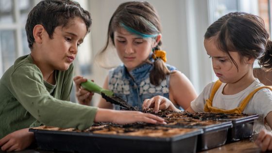 Three children are sat at a table together planting seeds.