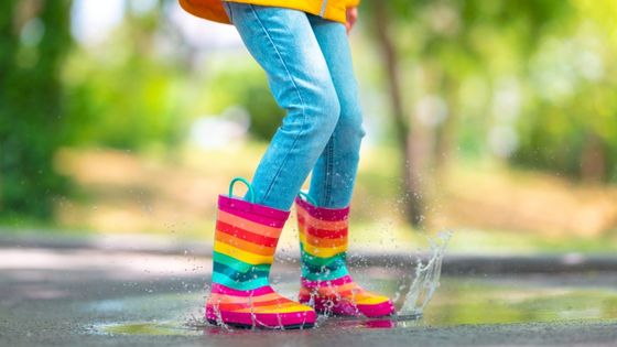 Image shows a child in rainbow striped wellington boots jumping in a puddle.