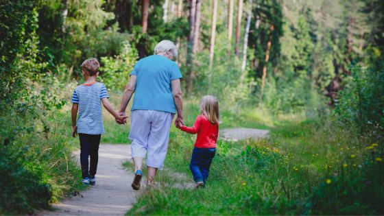 Image shows a grandmother walking down a forest path with her two grandchildren.