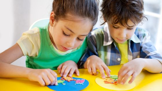 Two children are sat at a table making paper plate crafts.