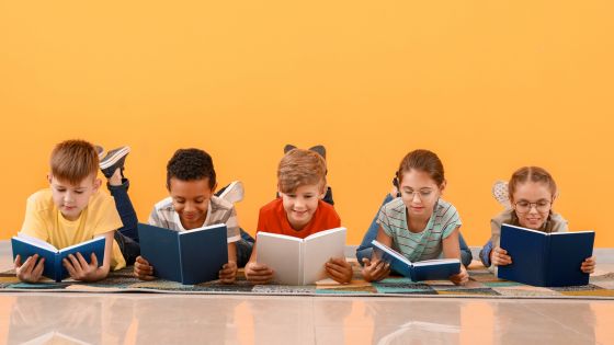Image shows five children laid on their tummies on the floor, each looking at a book.