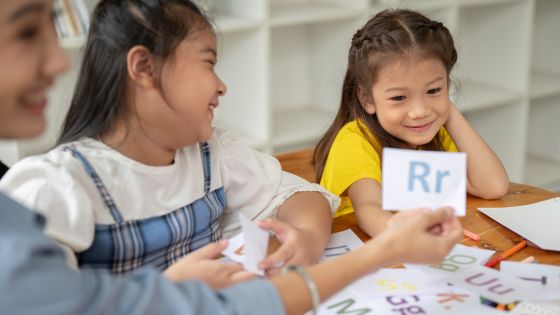 An adult and two children smiling together as they sit at a table sorting out English letter cards.