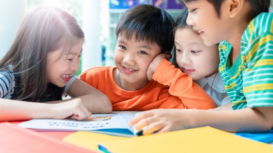 Four children are huddled around a book smiling together.