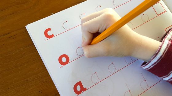 A child's hand is holding a pencil and is tracing over English lowercase letters in a workbook.