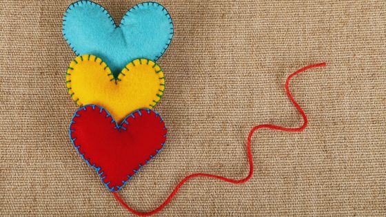 A picture of three felt sewn hearts, one is blue, the second is yellow, the third is red. They are each sitting behind each other.
