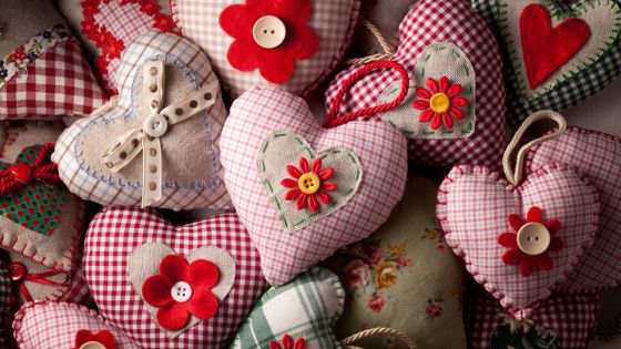 Many fabric sewn heart hangers with patterns of red and flowers and buttons on top.
