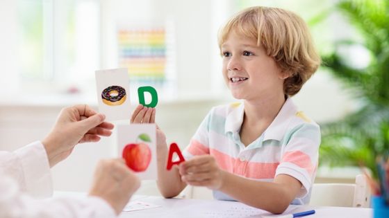 A picture of a boy holding up the letters A and D to match a woman's hands holding flashcards of a doughnut and an apple.