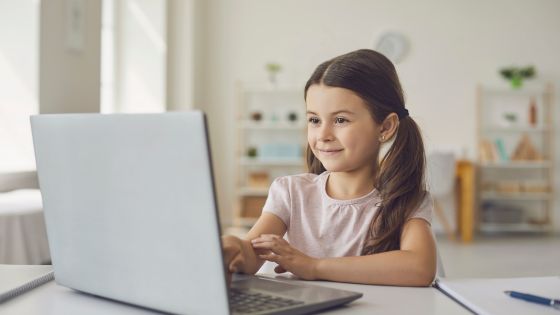 The image shows a photo of a girl sat at a desk with a laptop.