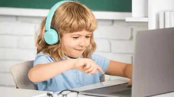 a child is sat with blue headphones and interacting on a laptop