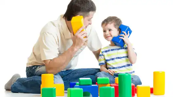 Father and son role playing together using coloured blocks as pretend phones