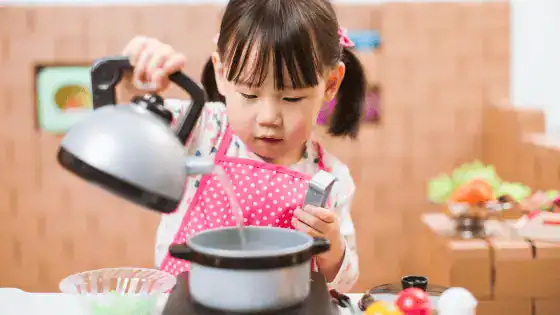 A young girl is role playing a chef with a toy kettle and pan.