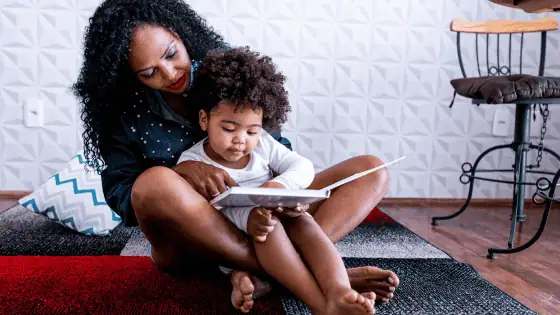 A mother is sat with her child in her lap reading a story together.