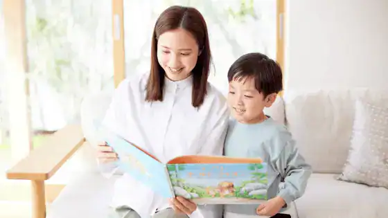 a mother and her son sat together smiling and reading a story book