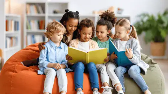Five children are sat in a library together looking at books.