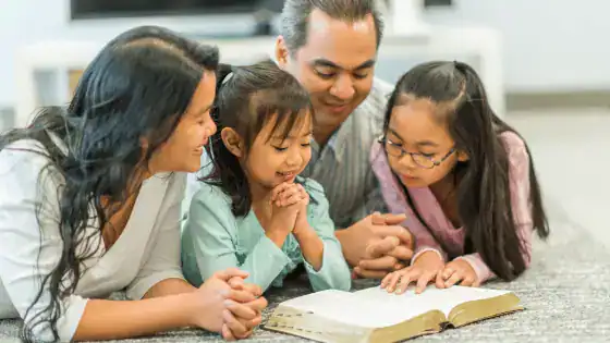 A family of four, mum, dad, and two girls, sat together looking at an open book.