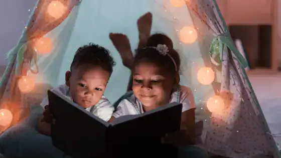 Two children are in a den looking at a bedtime story together