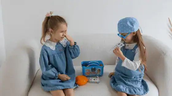 two young girls are sitting on the sofa pretending to play doctors