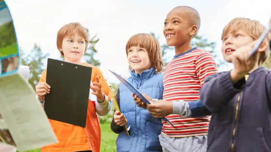 A group of 4 children outside with clip boards listening to a teacher ready to search for something.