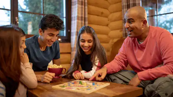 family of four sat in a cabin together in winter playing a board game