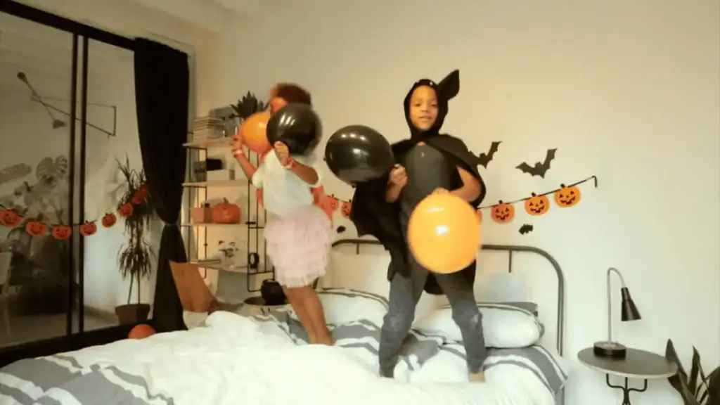 Kids dressed up for Halloween jumping on a bed with balloons and halloween decorations behind them